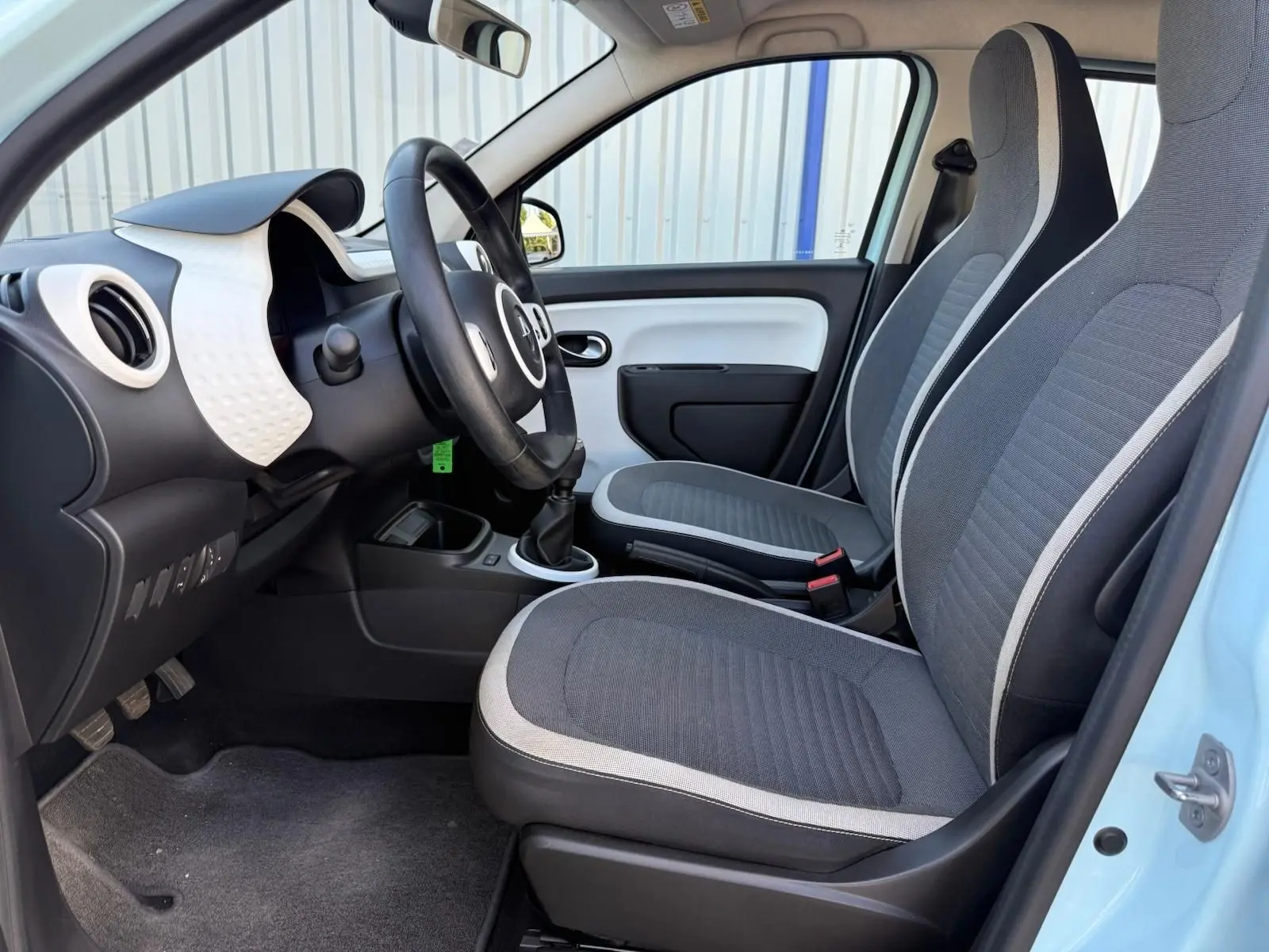 Intérieur avant droit de la Renault Twingo III bleu dragée 2021 avec sièges tissu gris et volant noir.