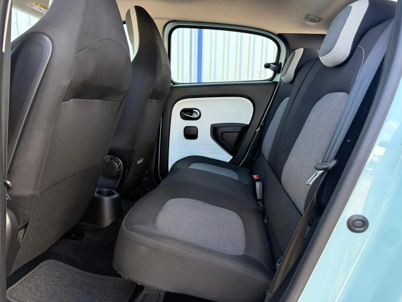 Vue latérale droite de l'habitacle arrière de la Renault Twingo III bleu dragée avec sièges bicolores gris et noir.