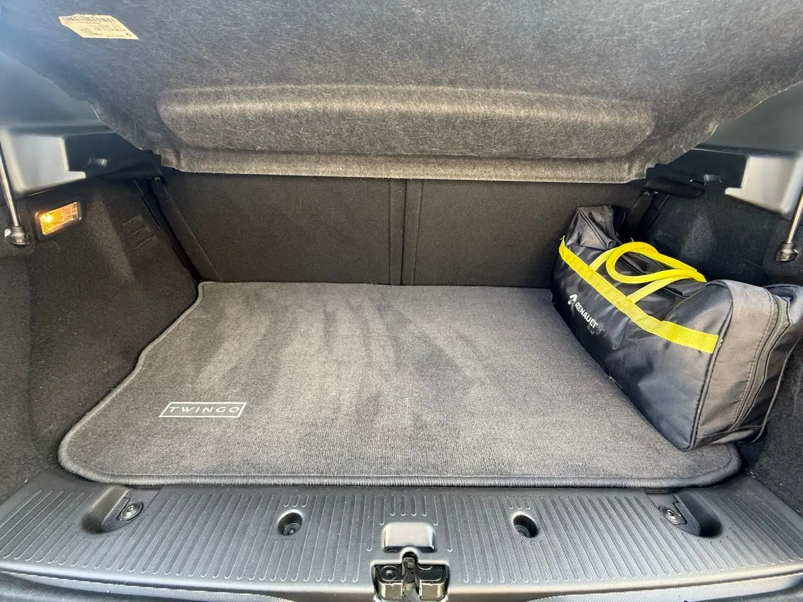 Coffre ouvert d'une Renault Twingo III bleu dragée, avec tapis gris marqué Twingo et sac de secours noir à liseré jaune.