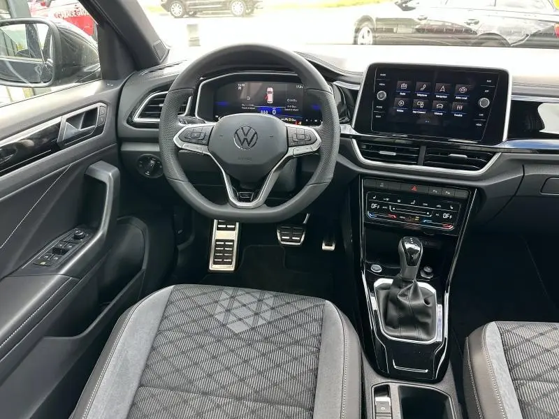 Intérieur du Volkswagen T-Roc 2025, vue frontale du poste de conduite avec volant multifonction et écran tactile central.