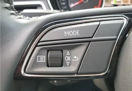 Gros plan sur les commandes au volant en plastique noir brillant de l'Audi A4 Avant Business 30 TDI gris Terra de 2020.