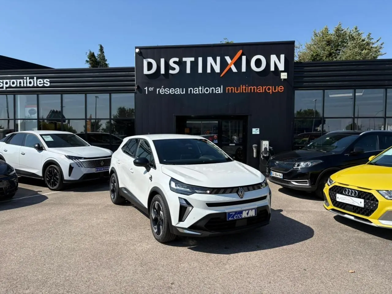 Renault Symbioz blanc nacré en 3/4 avant droit, avec calandre noire et jantes 18 pouces devant un showroom Distinxion.