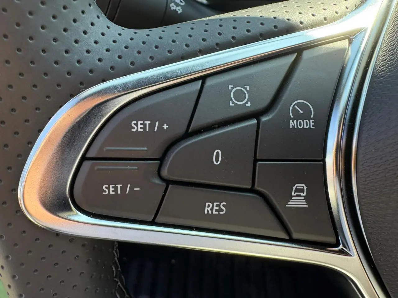 Gros plan sur les commandes de régulateur de vitesse au volant perforé du Renault Symbioz blanc nacré.