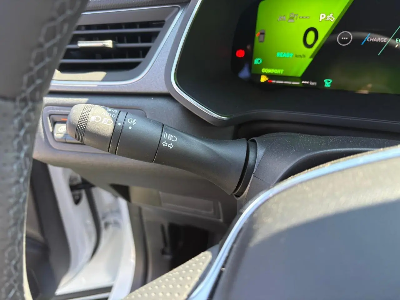 Gros plan sur la manette des feux et clignotants à gauche du volant d'une Renault Symbioz blanc nacré, tableau de bord numérique vert.