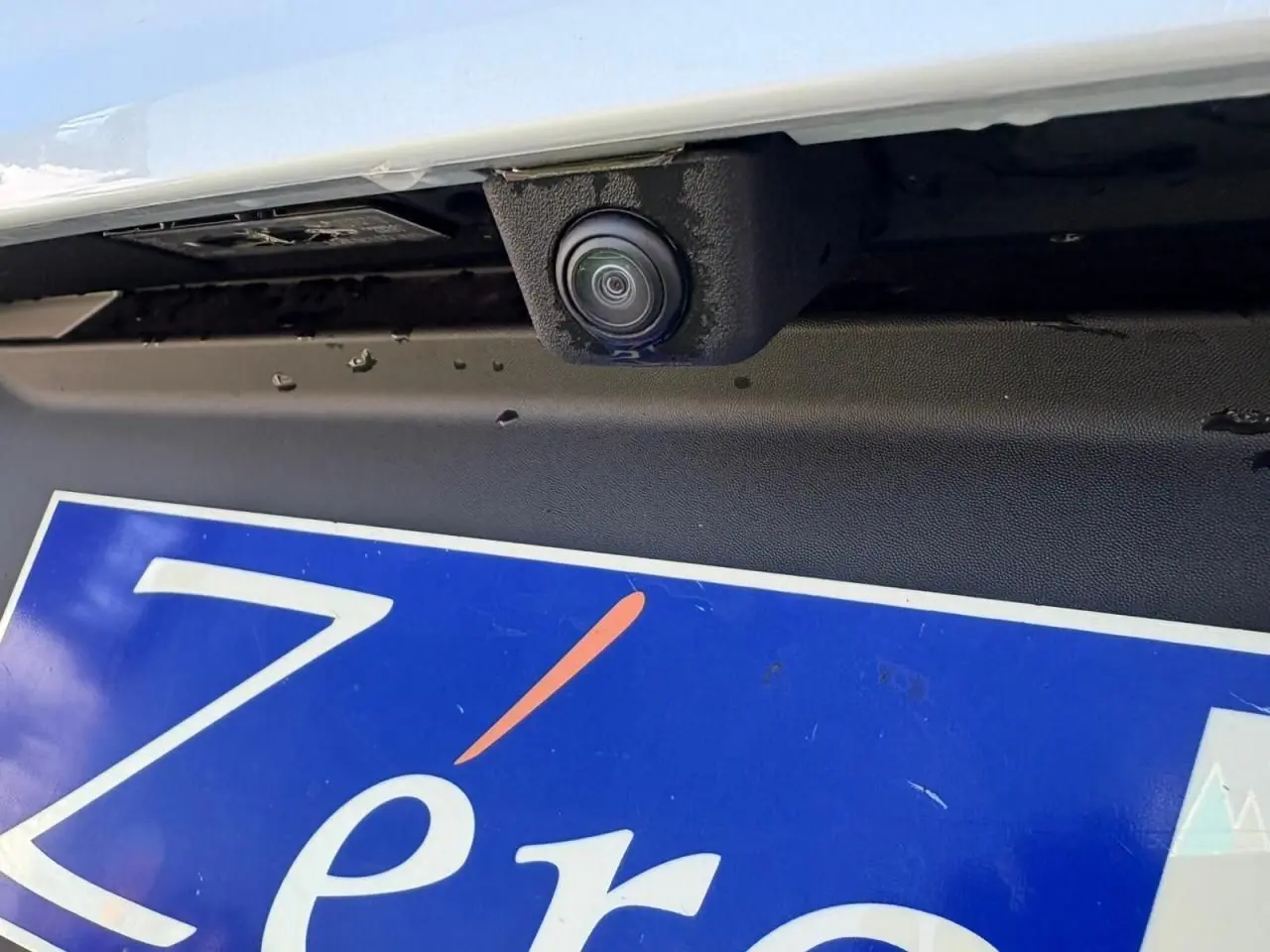 Gros plan sur la caméra de recul sous le pare-chocs arrière d'une Renault Symbioz blanc nacré.