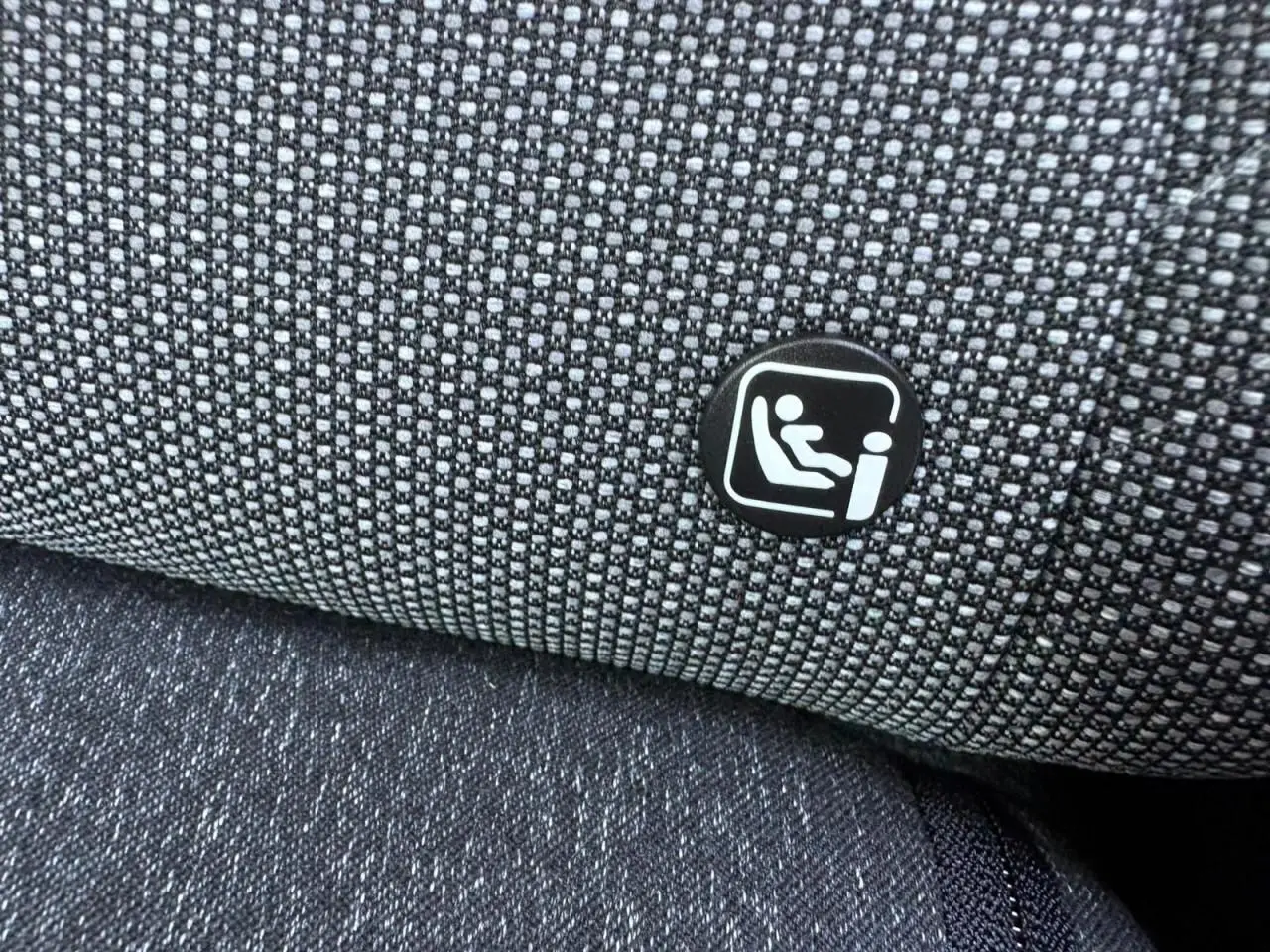 Gros plan sur le tissu gris du siège arrière avec l'icône du système Isofix visible sur la Renault Symbioz blanche nacrée.