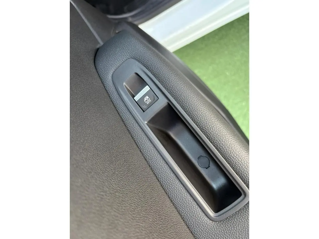 Gros plan sur le bouton de lève-vitre électrique côté gauche d'une Renault Symbioz blanc nacré avec intérieur noir.