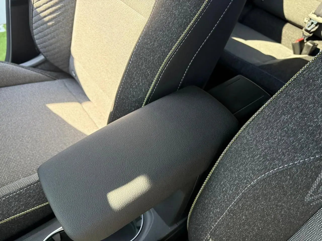 Accoudoir central noir entre les sièges avant gris avec surpiqûres vertes d'une Renault Symbioz 2025.