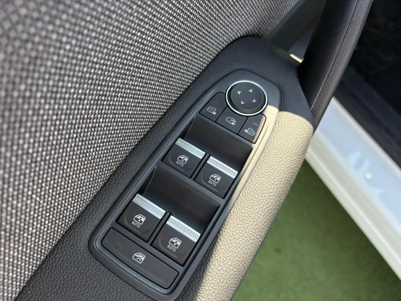 Panneau de commandes des vitres côté gauche en tissu gris, avec portière blanche nacrée visible en arrière-plan.