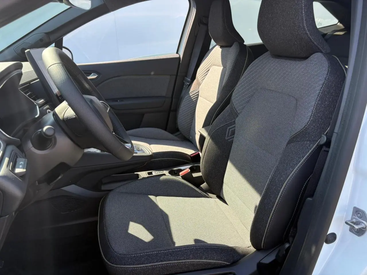 Vue intérieure côté gauche de la Renault Symbioz 2025 blanc nacré, sièges tissu gris avec volant et console centrale visibles.