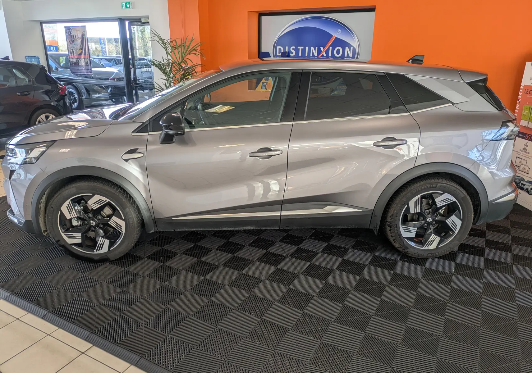Vue 3/4 avant d'un Renault Symbioz gris cassiopée métal, avec calandre lumineuse et jantes bi-ton distinctives.