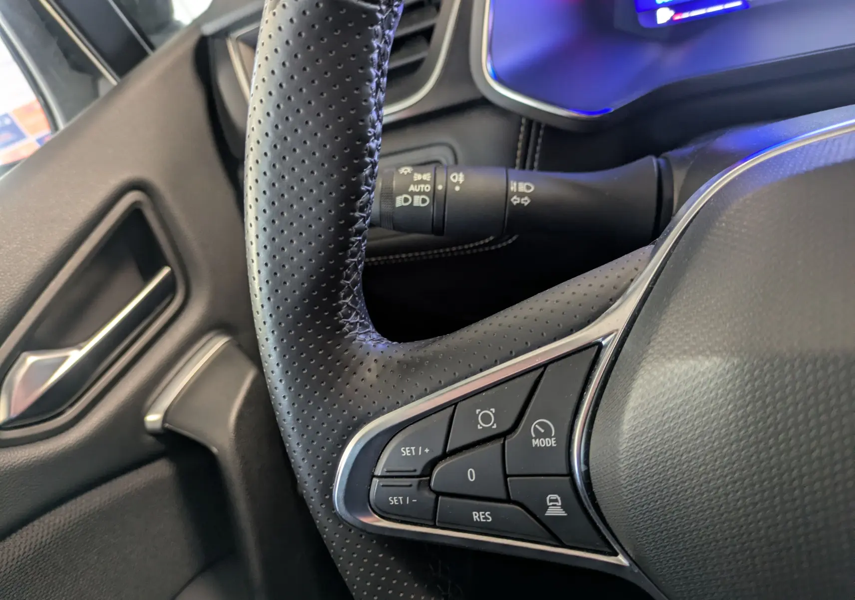 Gros plan sur le volant en cuir perforé du Renault Symbioz 2025, avec commandes intégrées et tableau de bord numérique partiellement visible.