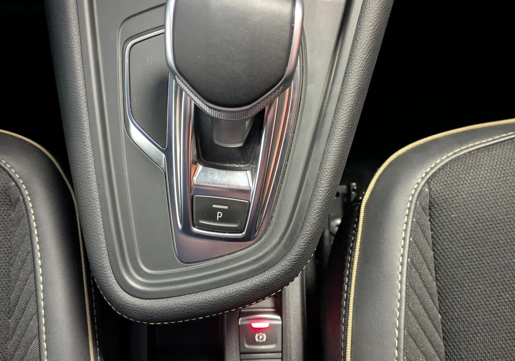Vue plongeante sur la console centrale intérieure du Renault Symbioz 2025, avec levier de vitesse noir et sièges tissu gris à surpiqûres beiges.