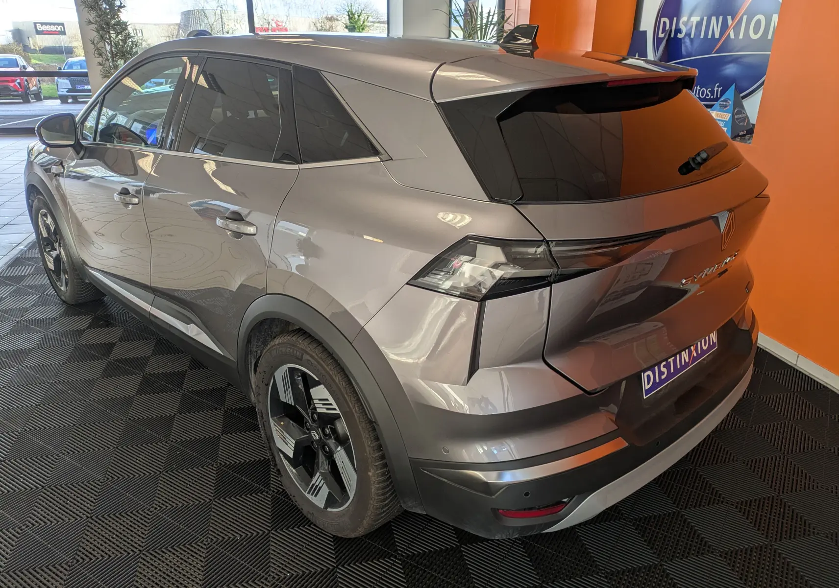Vue 3/4 arrière droite d’un Renault Symbioz gris cassiopée métal avec vitres teintées et jantes noires en concession.