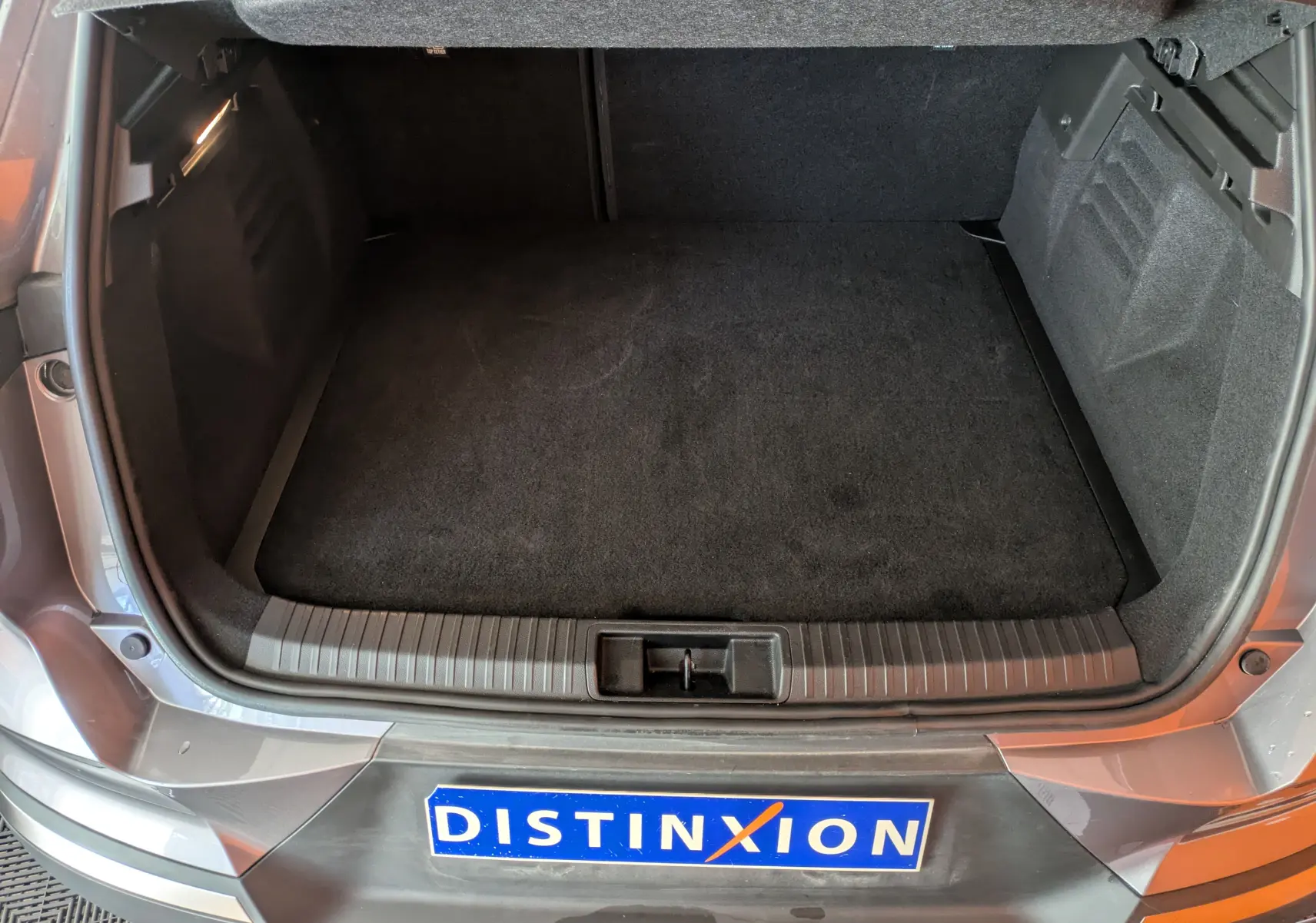 Coffre ouvert vu de dessus sur Renault Symbioz gris cassiopée métal, montrant l’espace de chargement vide et tapis noir.