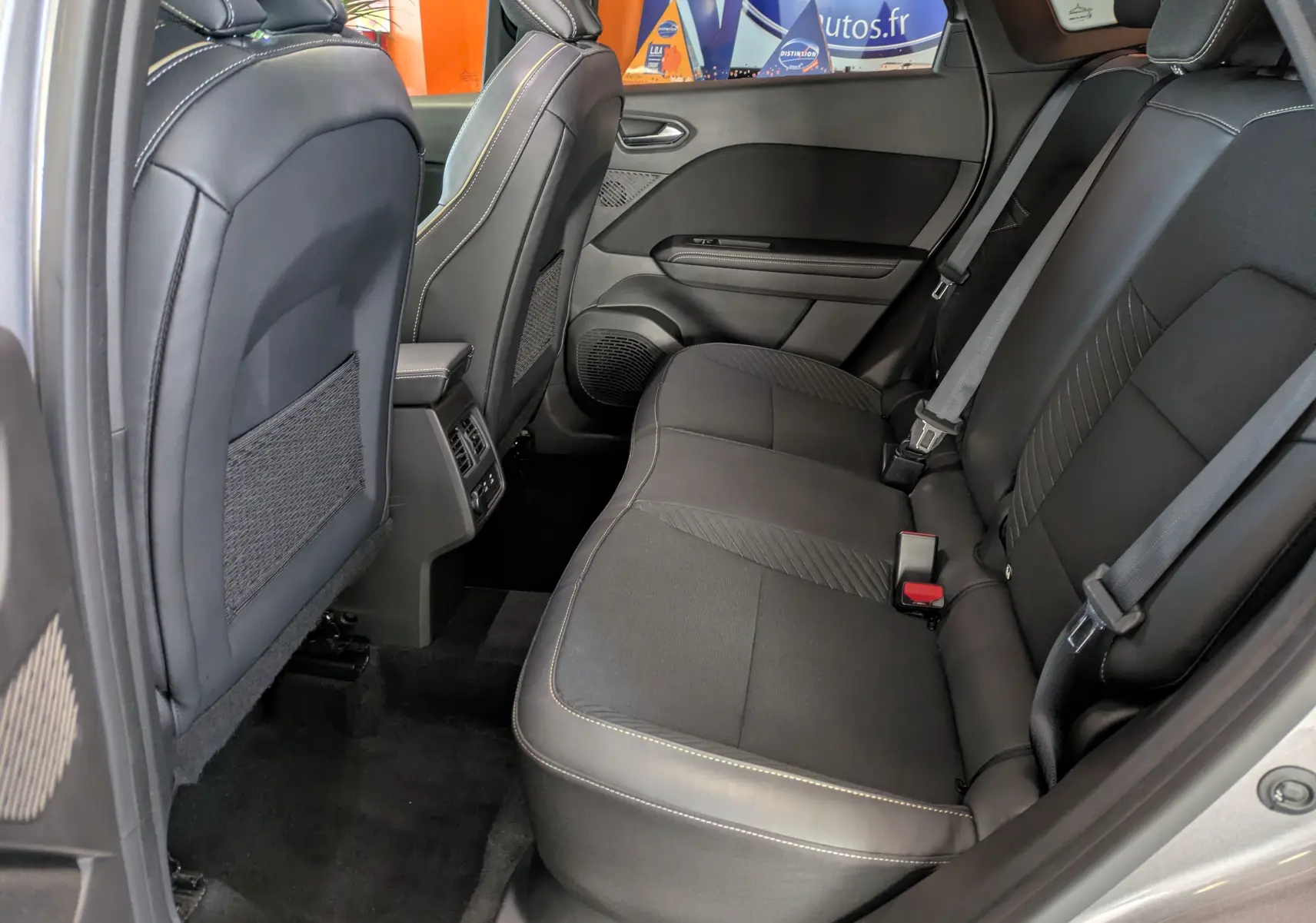 Vue intérieure arrière côté droit du Renault Symbioz 2025, sièges tissu noir avec surpiqûres claires et ceintures grises.