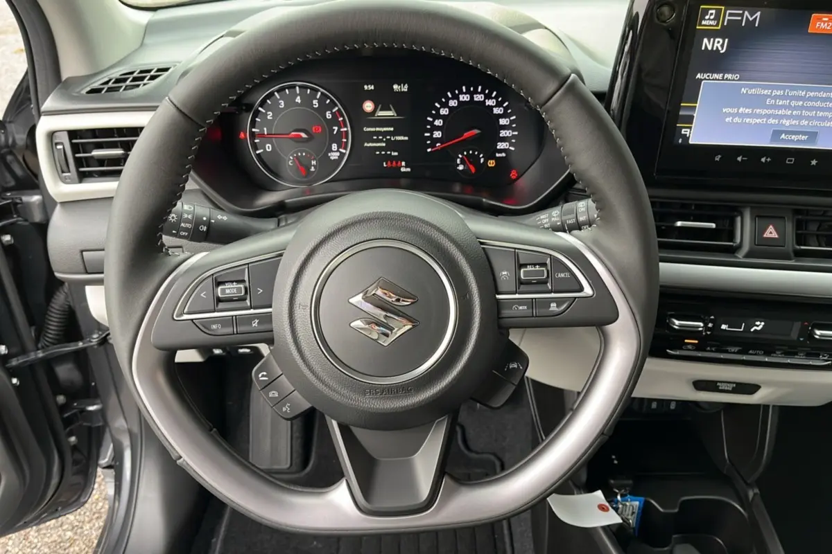 Vue centrée sur le volant cuir multifonctions d'une Suzuki Swift 2026, avec tableau de bord et écran tactile visible.