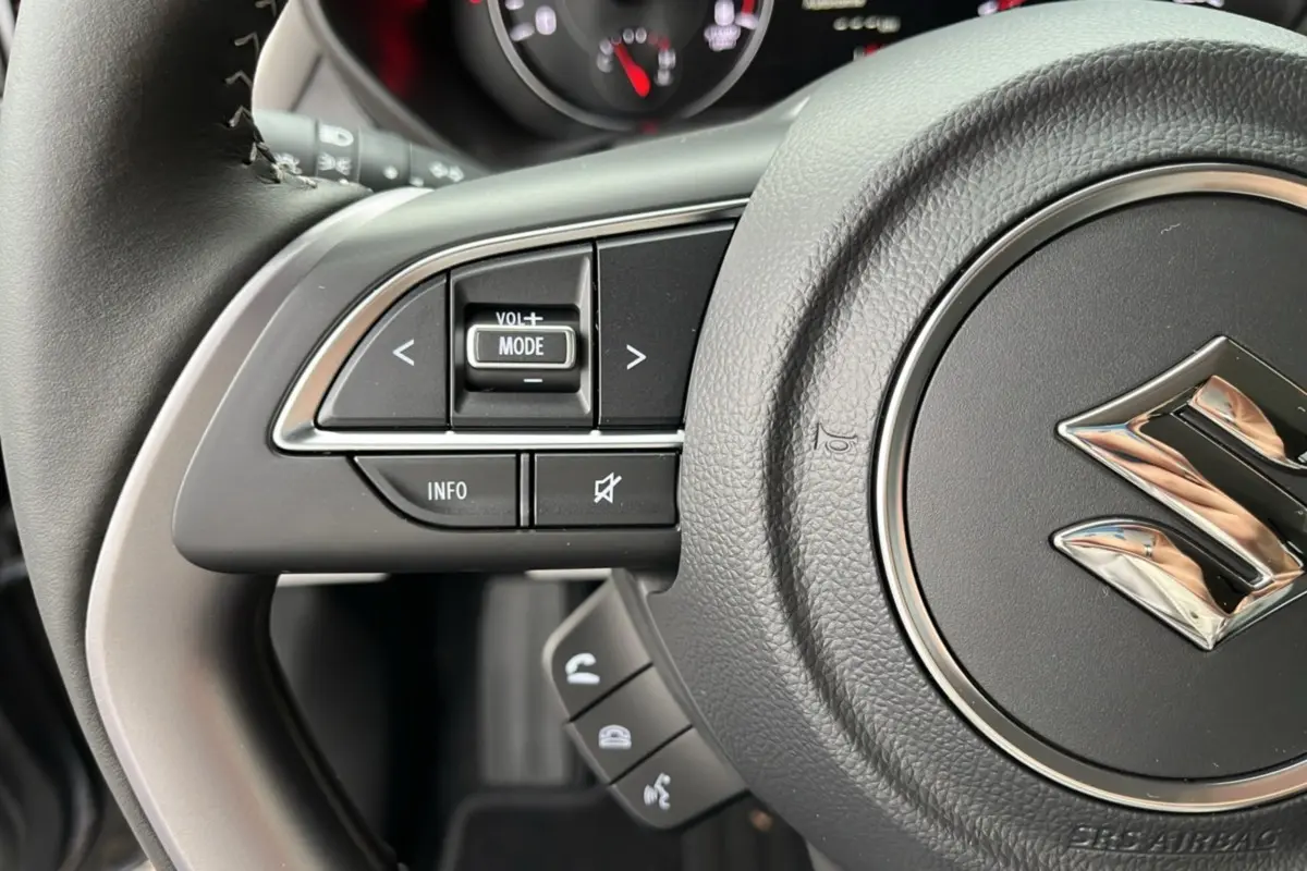 Gros plan sur le volant cuir gris de la Suzuki Swift 2026, avec commandes multifonctions et logo Suzuki central chromé.