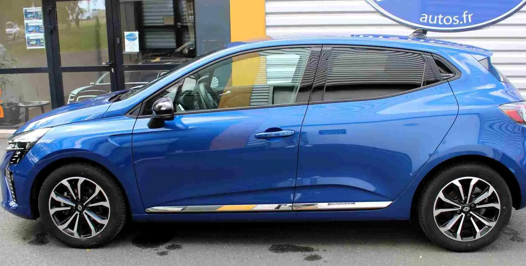 Vue intérieure avant de la Renault Clio hybride 2025, tableau de bord gris noir avec écran tactile central et volant multifonction.