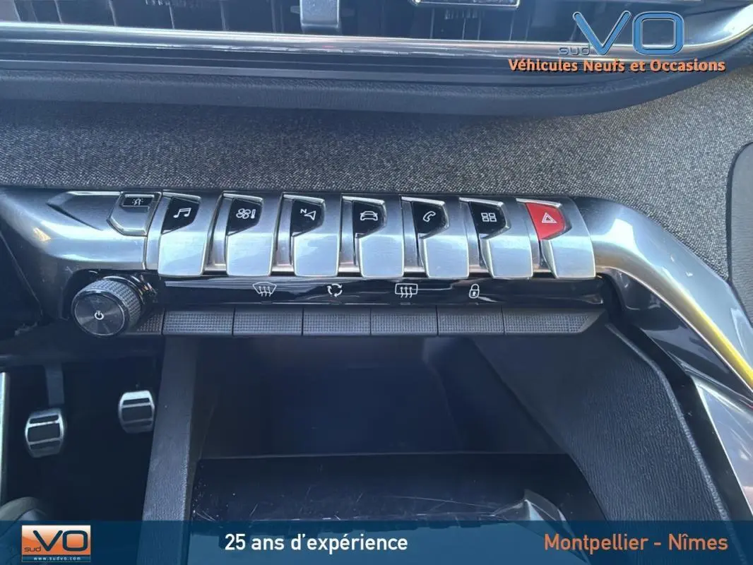 Gros plan sur la rangée de commandes chromées du tableau de bord du Peugeot 3008 gris foncé, avec pédales visibles en dessous.