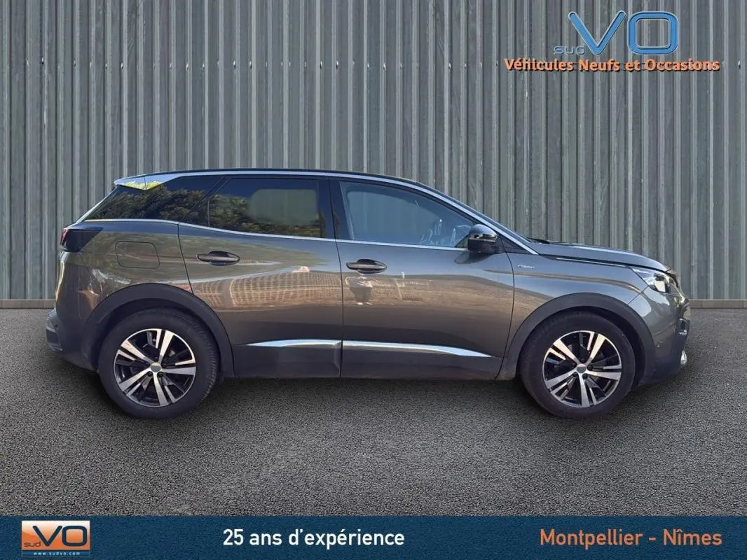 Profil côté droit du Peugeot 3008 gris foncé de 2018 avec jantes alliage 18 pouces, garé devant un mur métallique.
