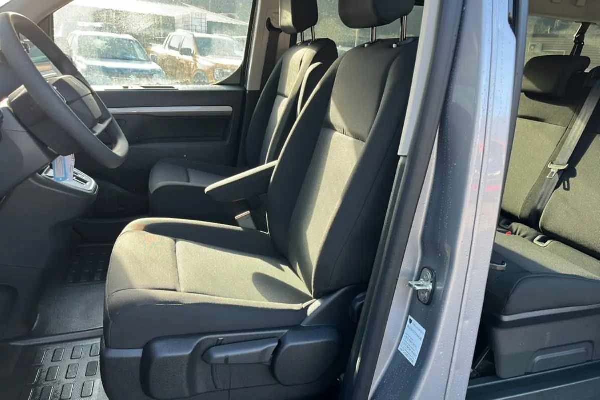Vue intérieure côté conducteur du Peugeot Traveller gris acier 2025, montrant les sièges avant avec accoudoir central.
