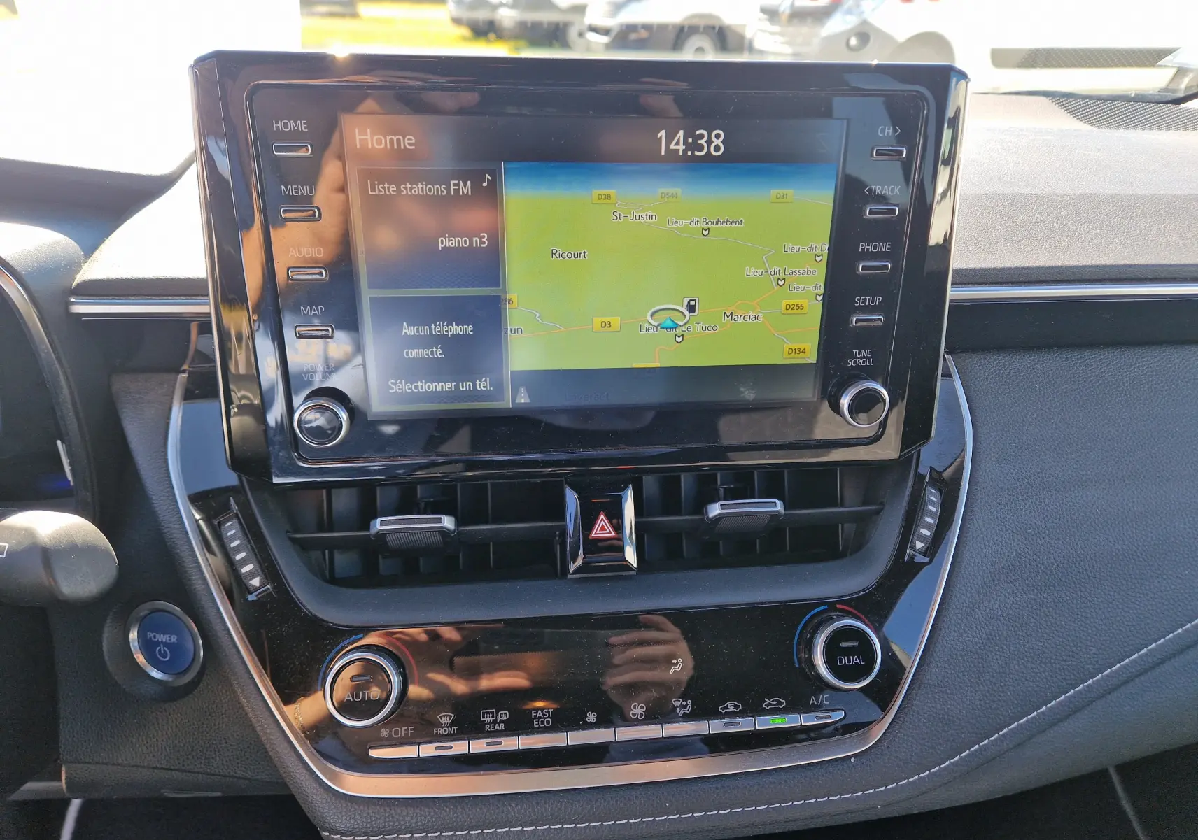 Vue rapprochée de l’écran tactile central et de la console de la Toyota Corolla Hybride 122h gris clair, avec commandes climatisation et bouton démarrage.