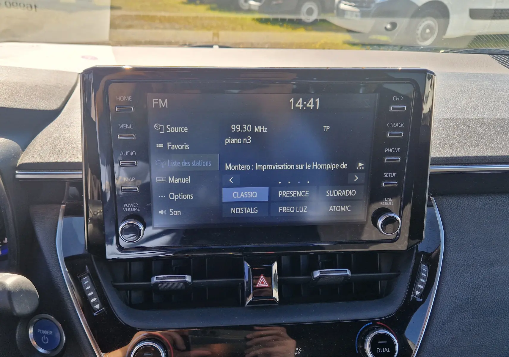 Vue rapprochée de l’écran multimédia central de la Toyota Corolla Hybride 122h gris clair métal, affichant la radio FM.