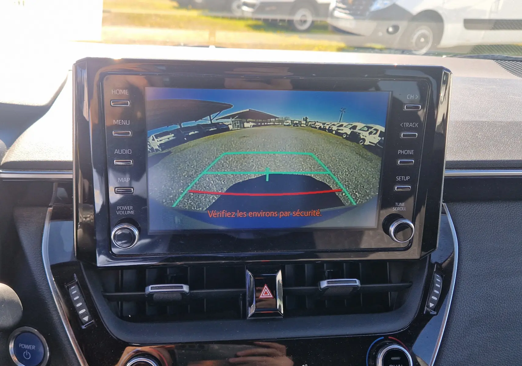 Vue intérieure centrée sur l'écran multimédia affichant la caméra de recul d'une Toyota Corolla hybride gris clair de 2019.