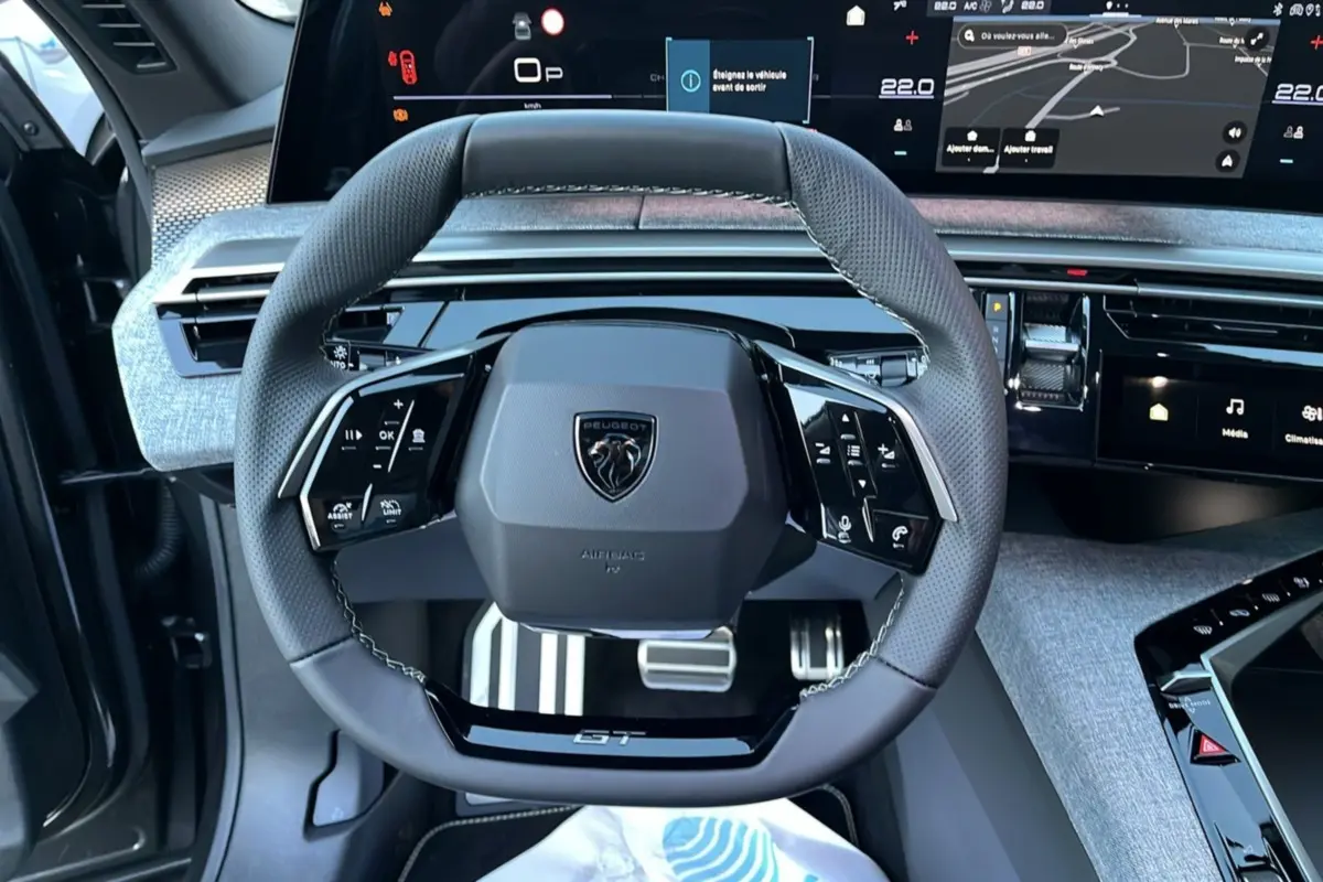 Vue rapprochée du volant cuir multifonctions Peugeot 5008 Hybrid 145 GT Alcantara avec tableau de bord numérique et finition grise.