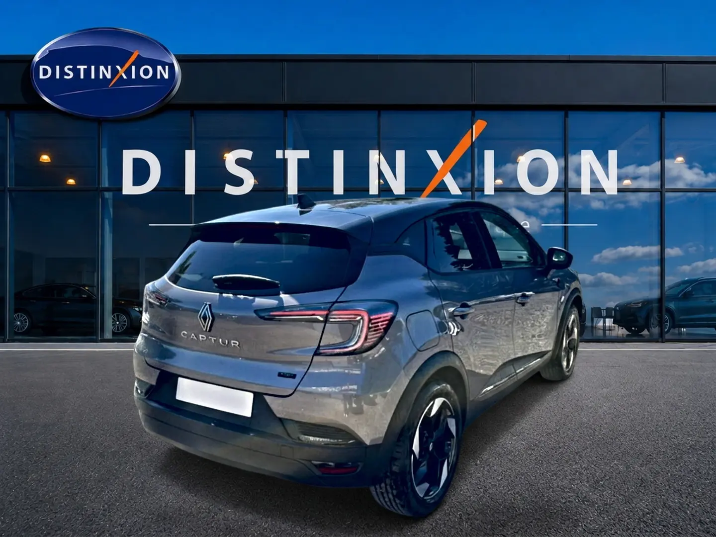 Vue 3/4 arrière droite du Renault Captur gris cassiopée devant une vitrine avec logo Distinxion.