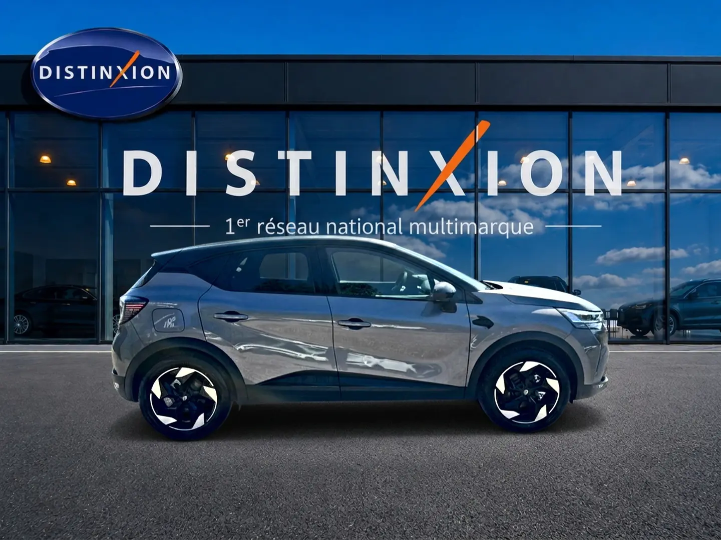 Renault Captur gris cassiopée en profil droit devant une vitrine avec logo Distinxion, jantes alu noires et blanches.