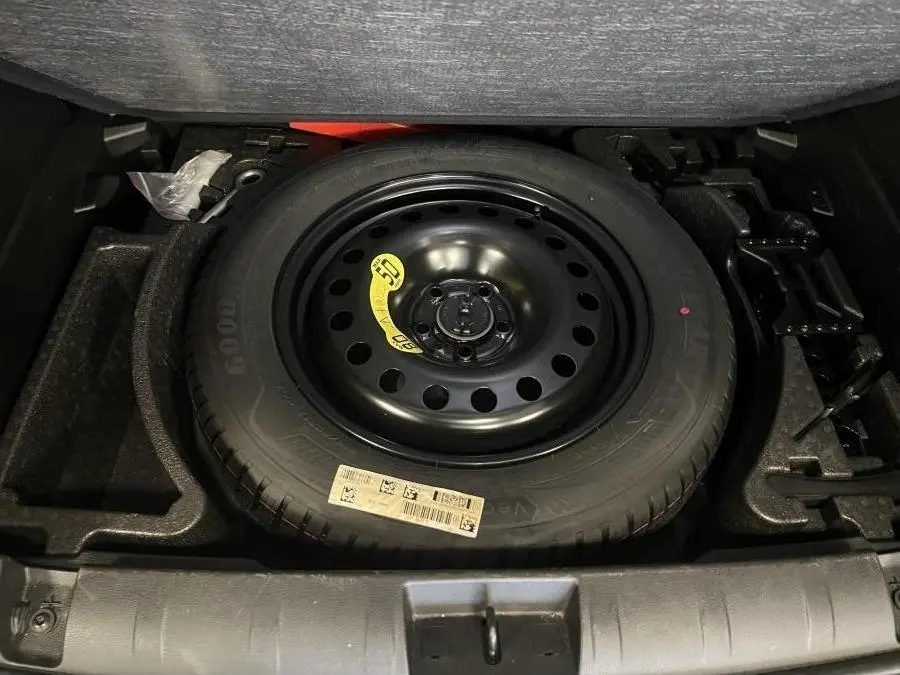 Roue de secours temporaire noire dans le coffre du Jeep Renegade gris 2024, avec plancher modulable visible.