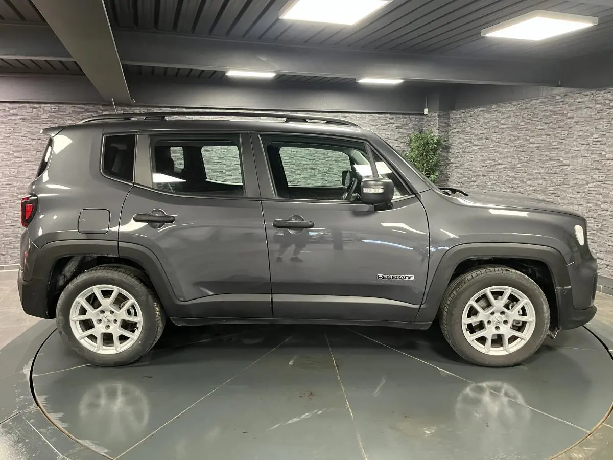 Profil côté gauche d'un Jeep Renegade gris métallisé 2024 avec jantes alliage 17 pouces et barres de toit noires.