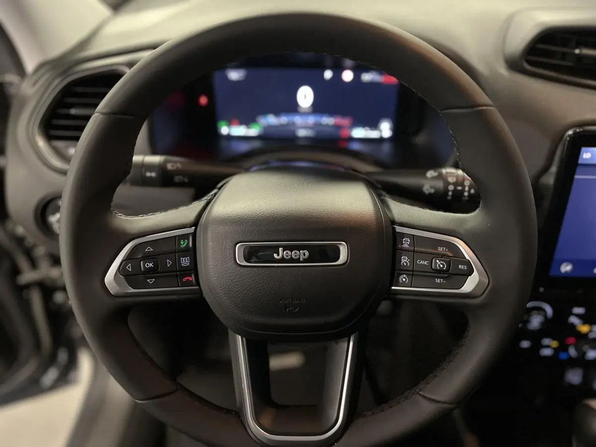 Volant noir Jeep Renegade 2024 avec commandes intégrées, tableau de bord numérique et écran tactile visible en arrière-plan.