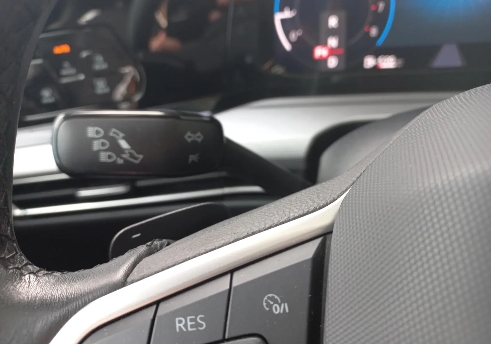 Gros plan sur la commande de régulateur de vitesse au volant d'une Volkswagen Golf gris dauphin 2023, intérieur moderne.