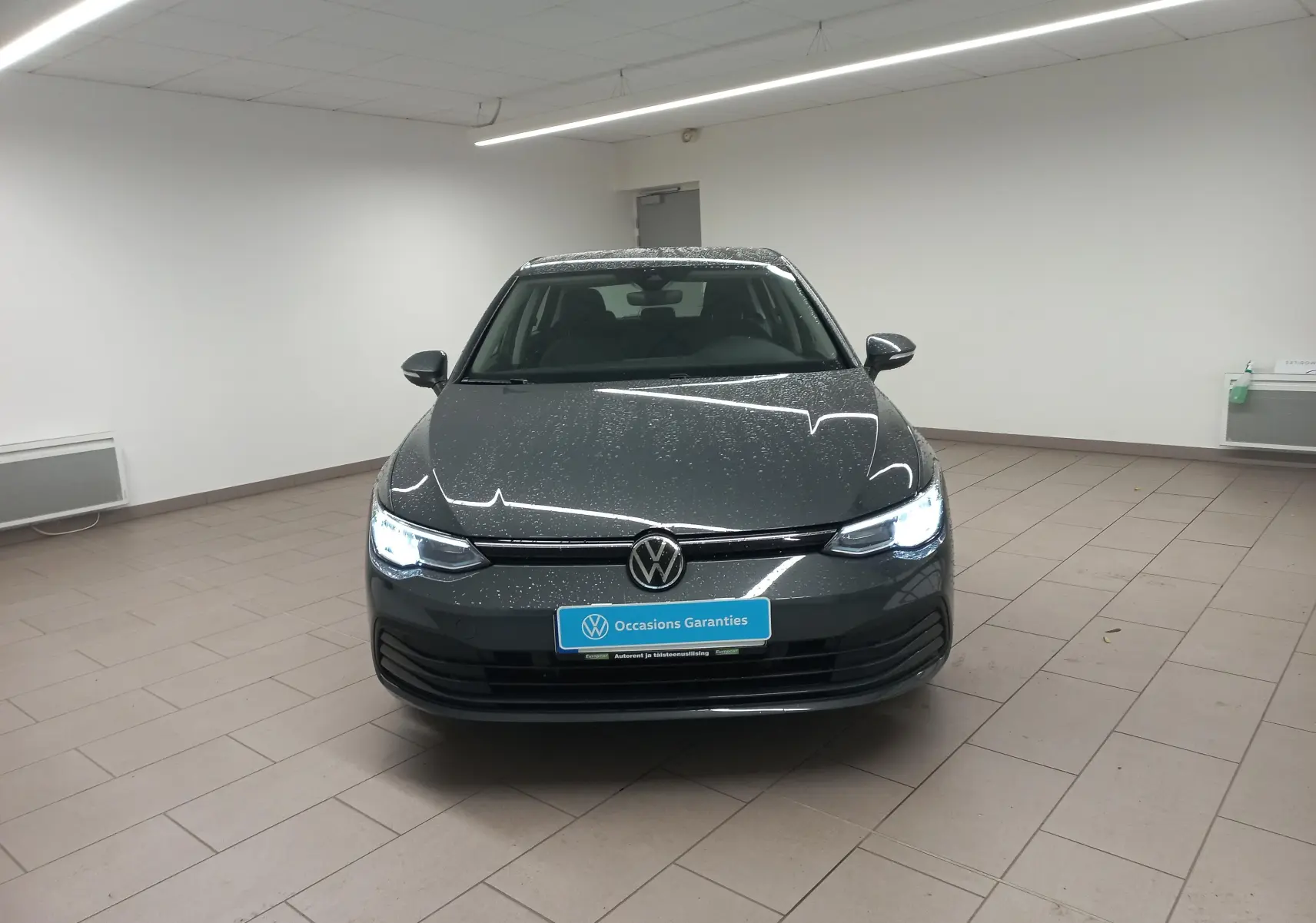 Volkswagen Golf 1.5 TSI gris dauphin vue avant avec phares allumés dans un showroom lumineux.
