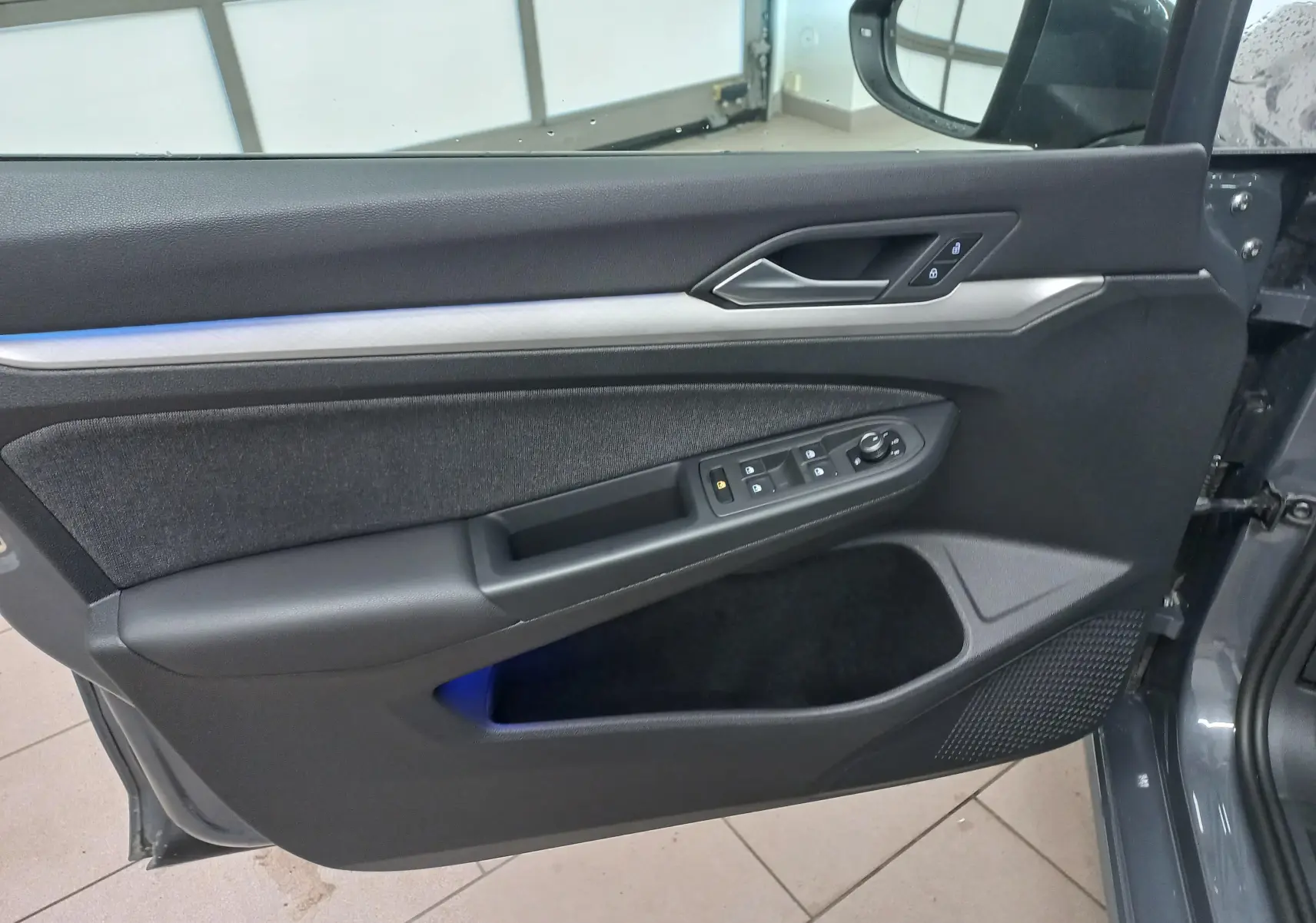 Vue intérieure de la porte avant gauche d'une Volkswagen Golf 1.5 TSI gris dauphin avec commandes électriques et éclairage d'ambiance bleu.