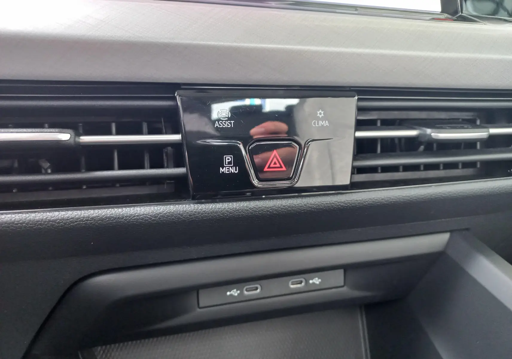 Gros plan sur la console centrale de la Volkswagen Golf gris dauphin 2023, avec boutons d'alerte et ventilation.