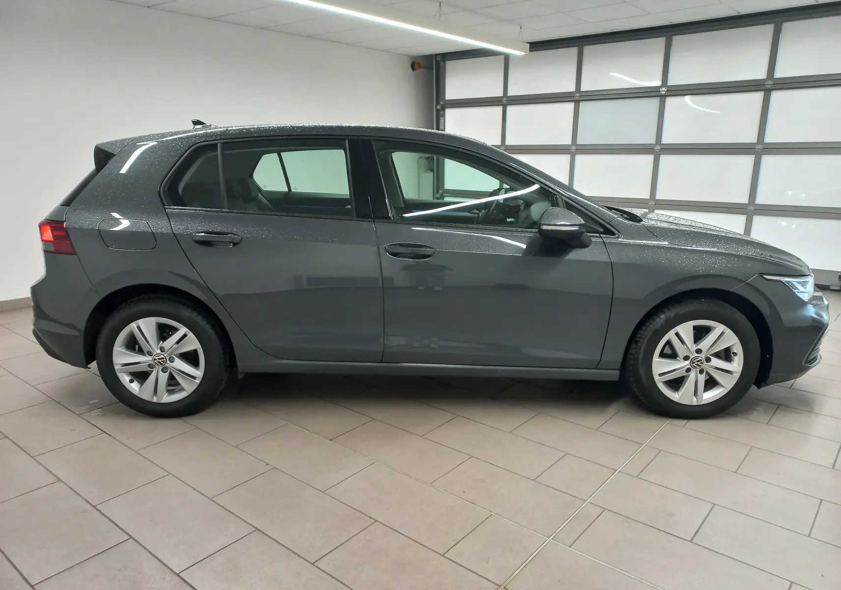 Profil droit d'une Volkswagen Golf 1.5 TSI 130 DSG7 Life Plus gris dauphin métallisé, en intérieur avec pluie sur la carrosserie.