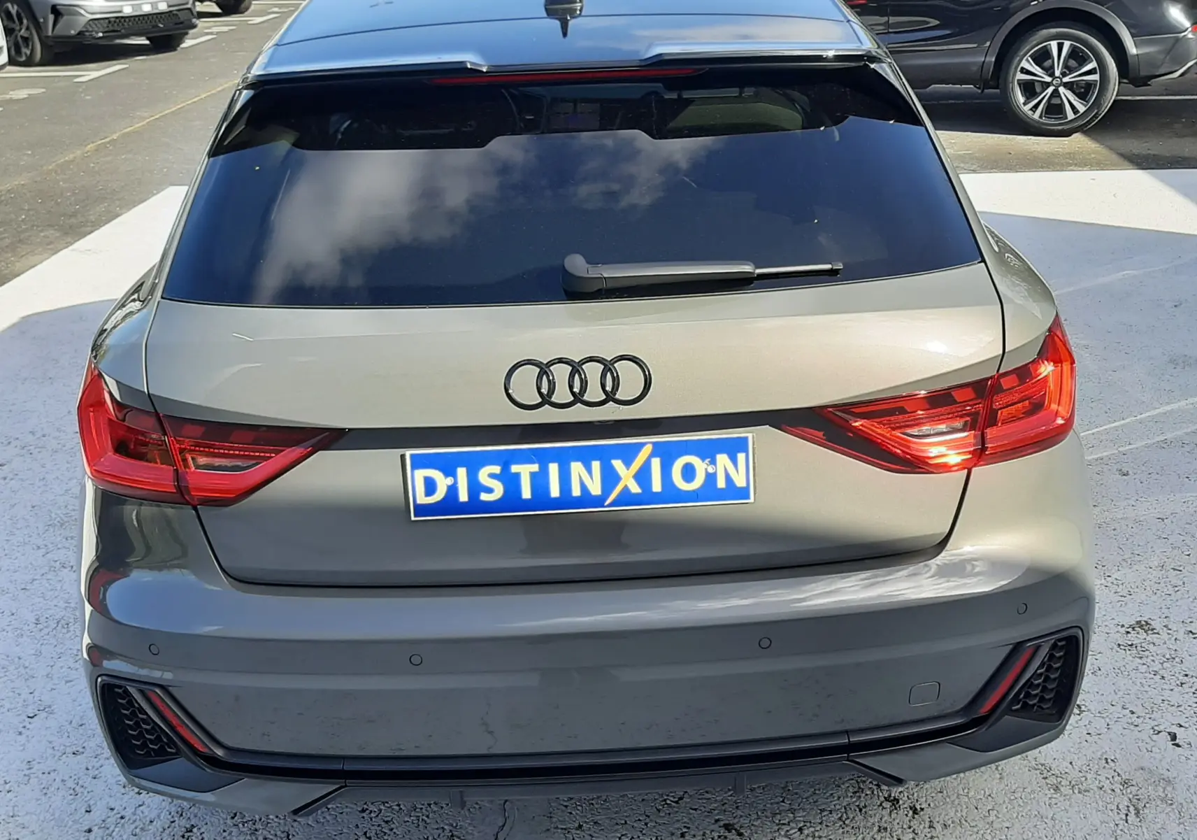 Vue arrière d'une Audi A1 Sportback gris Chronos avec toit noir, vitres arrière surteintées et feux LED allumés.