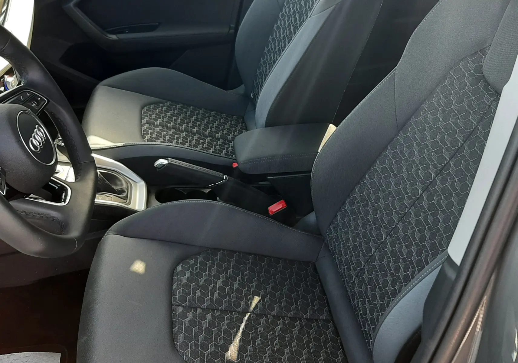 Vue intérieure côté conducteur de l'Audi A1 Sportback 2025, sièges tissu gris noir avec motifs hexagonaux et volant cuir.
