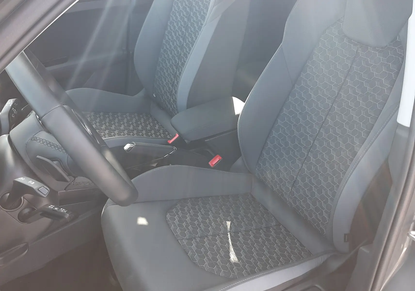 Vue intérieure côté conducteur de l'Audi A1 Sportback 2025, sièges tissu gris avec motifs hexagonaux et volant cuir sport.