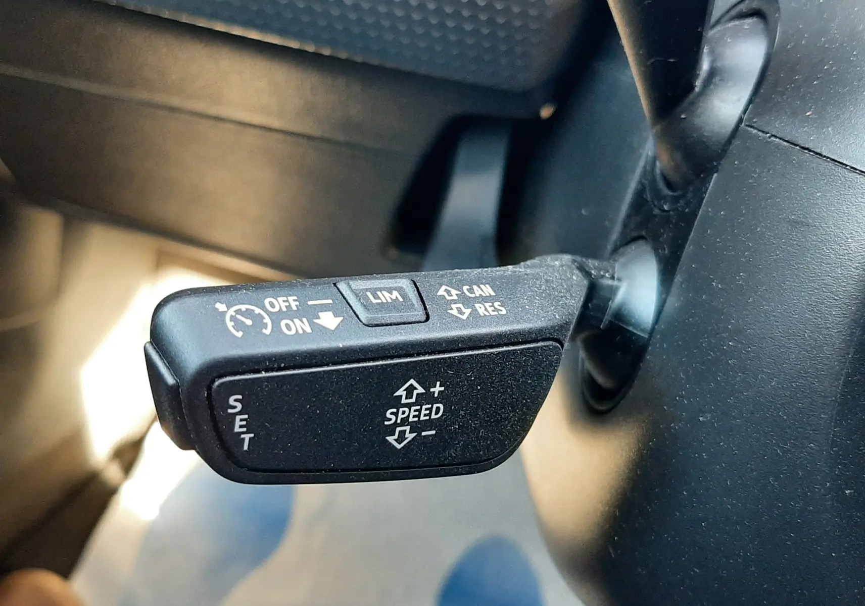 Gros plan sur la commande de régulateur de vitesse à gauche du volant d'un Audi A1 Sportback gris chronos 2025.