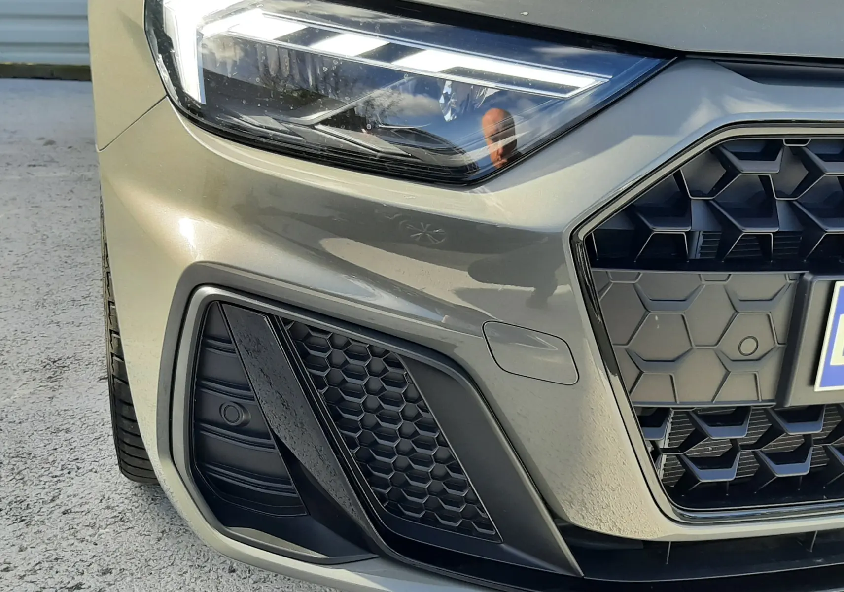 Gros plan sur l'avant gauche de l'Audi A1 Sportback gris Chronos, mettant en valeur le phare LED et la calandre hexagonale noire.