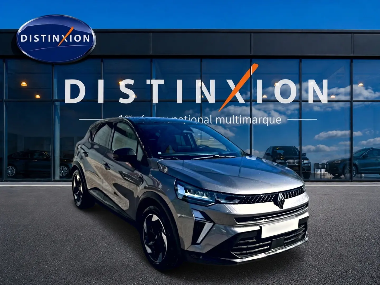 Renault Captur 2026 gris cassiopée en 3/4 avant, avec jantes alu et calandre distinctive, devant showroom Distinxion.