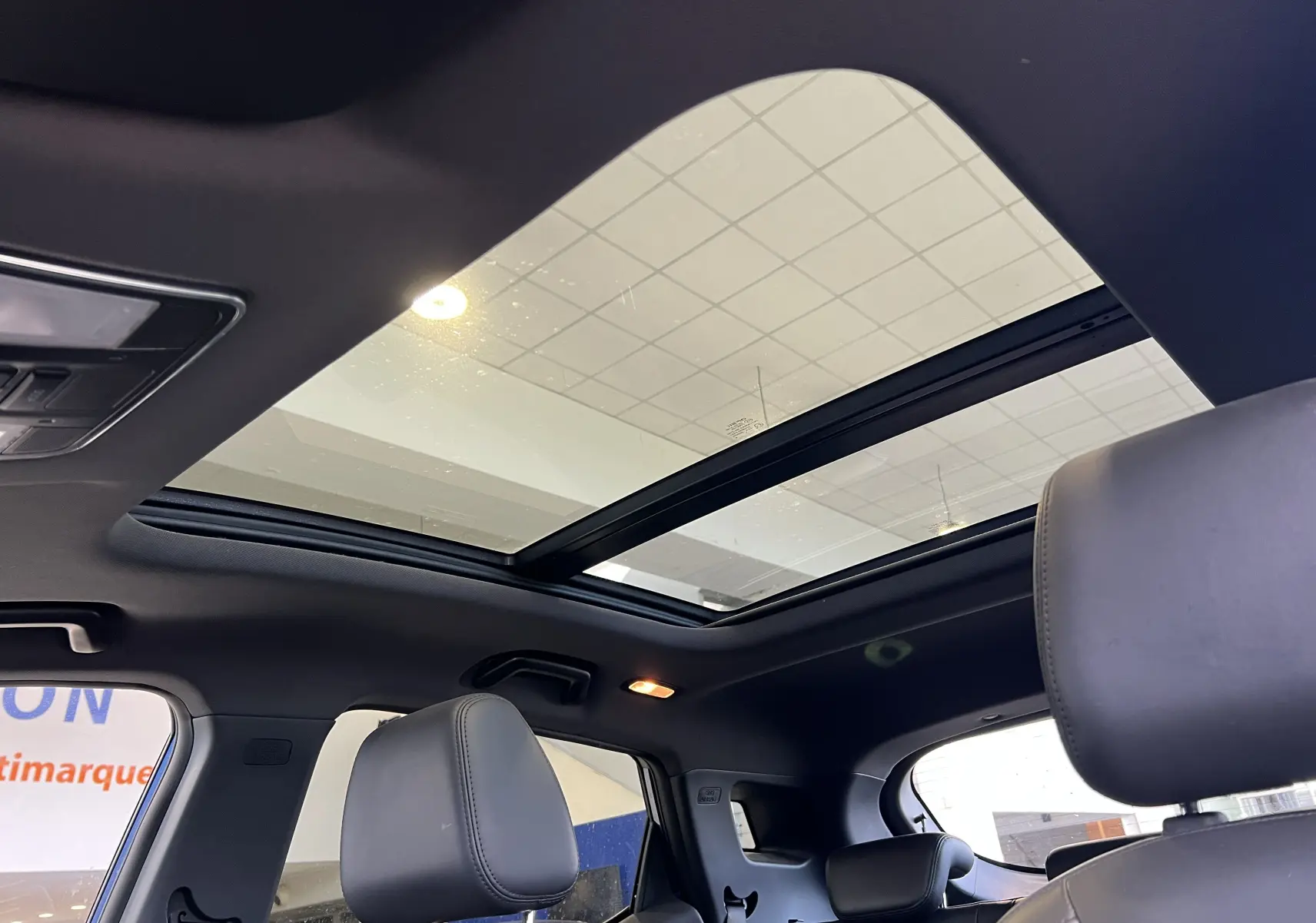 Toit panoramique ouvert vu de l'intérieur arrière du SERES 3 Electric 163ch Luxe avec sièges noirs et lumière ambiante.