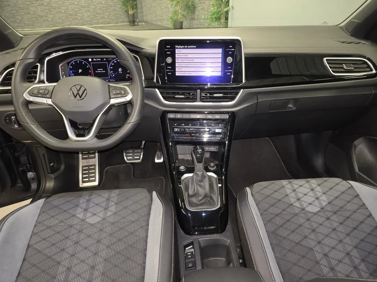 Vue intérieure frontale du tableau de bord et volant du Volkswagen T-Roc 1.5 TSI R-Line avec sellerie tissu et console noire brillante.
