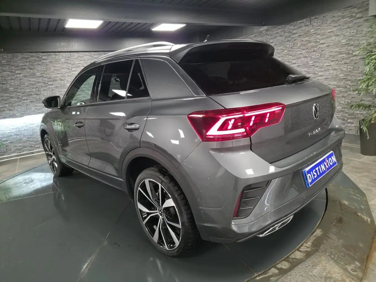 Vue 3/4 arrière droite d'un Volkswagen T-Roc gris métallisé avec feux LED allumés et jantes alliage noir et argent.