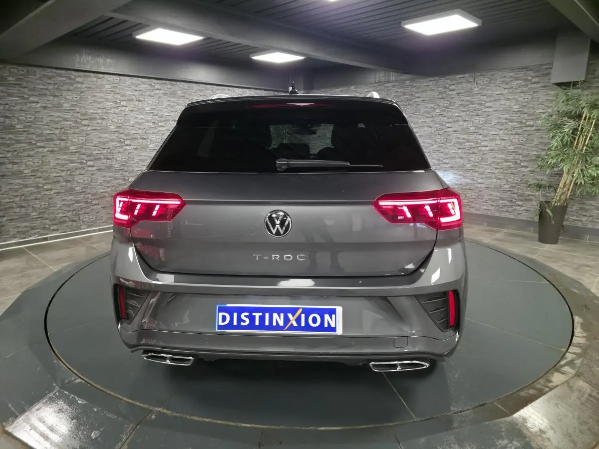 Vue arrière d'un Volkswagen T-Roc gris métallisé avec feux LED allumés et double sortie d'échappement chromée.